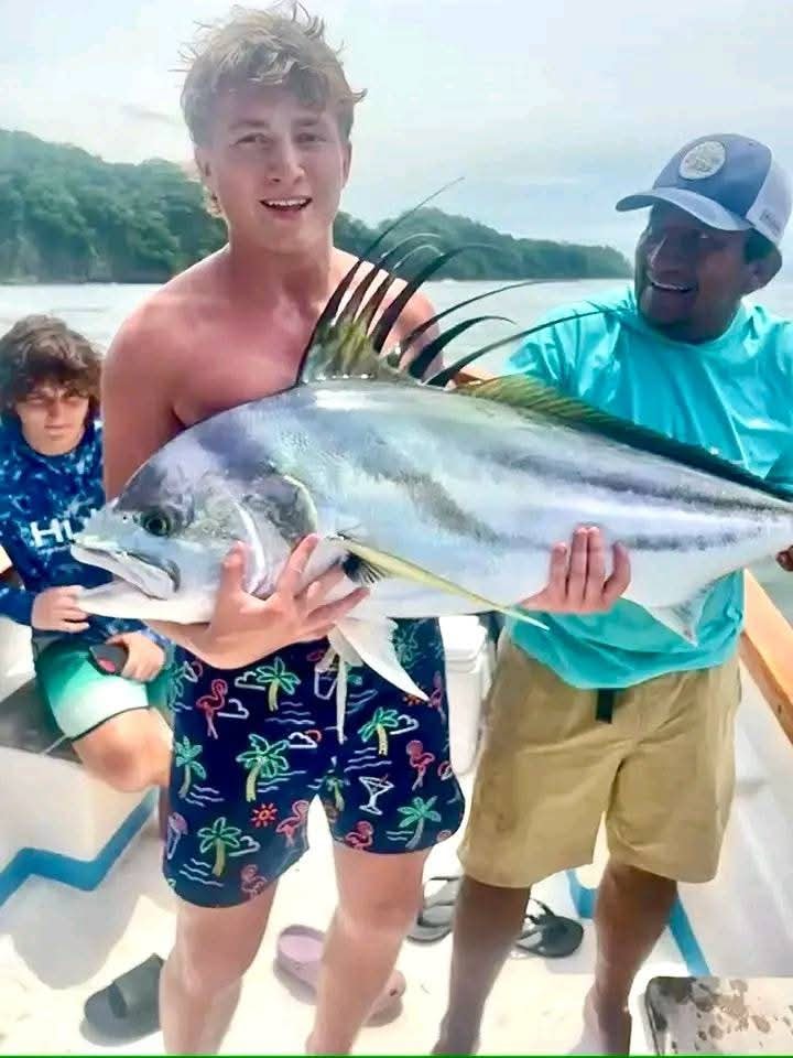 Happy angler holding a large roosterfish on a charter boat in Costa Rica